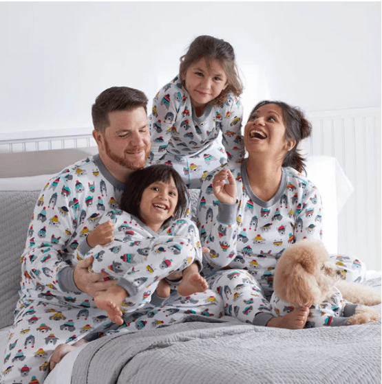 family of 4 (mom, dad, brother, sister) and dog all wearing long sleeved matching pajamas. The print features a variety of dogs wearing colorful beanie hats or sunglasses.