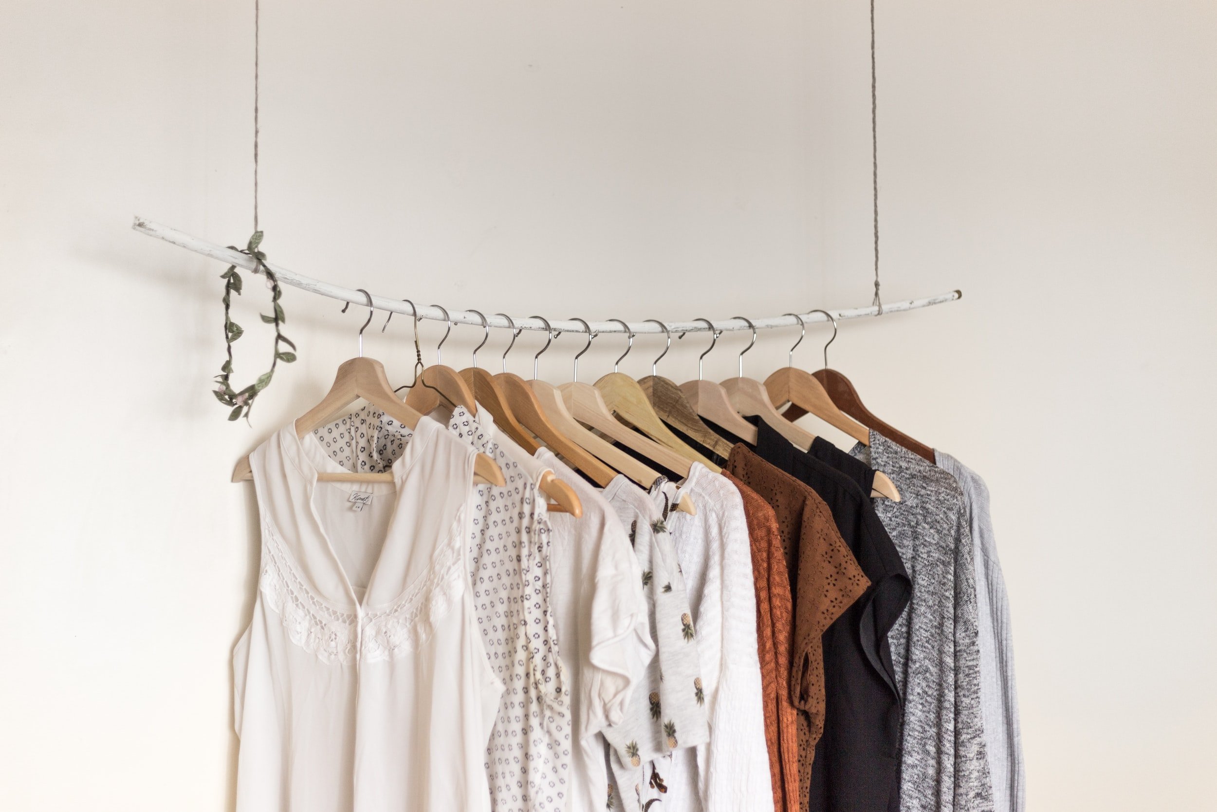 hanging branch that is being used as a clothes rod. many shirts and dresses, in neutral colors are hanging from it.